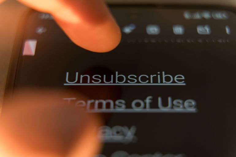 Close-up of a finger to tap the Unsubscribe link on a smartphone screen in dark mode. High quality photo