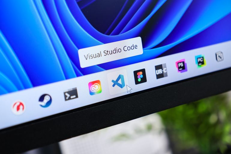 Poznan, Poland - June 6, 2025: A close-up view of the Visual Studio Code icon with a mouse cursor on a Windows 11 desktop taskbar, showing modern programming environment