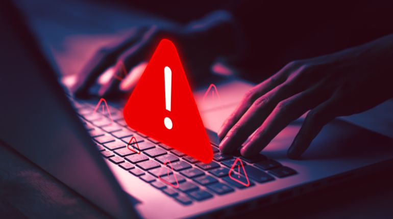 shutterstock_2702280107-1779100286-1 Cybersecurity warning with red alert sign on laptop, symbolizing online threat, hacking danger, virus alert, cyber attack, data protection, and digital security issues.