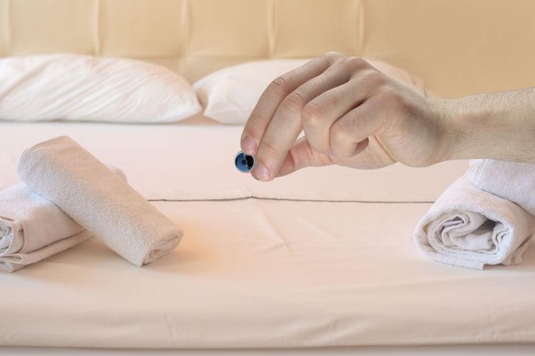 Hand gripping small security camera, portability and convenience, discreet monitoring, video surveillance inviting bedroom with fresh linens and neatly folded towels on bed, Hotel room interior