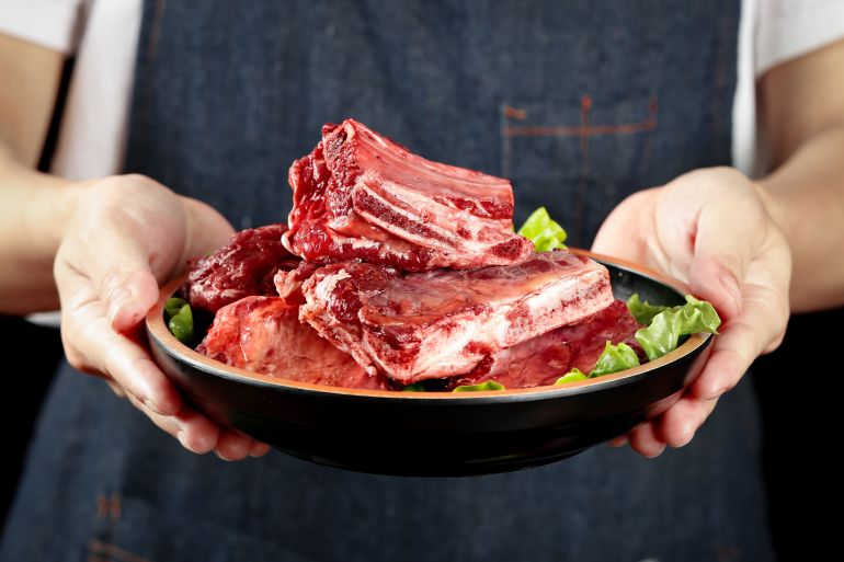Fresh raw beef ribs displayed on a black plate with green lettuce garnish, held by hands wearing dark apron. Premium quality inner Mongolia beef cuts suitable for grilling and BBQ meals.
