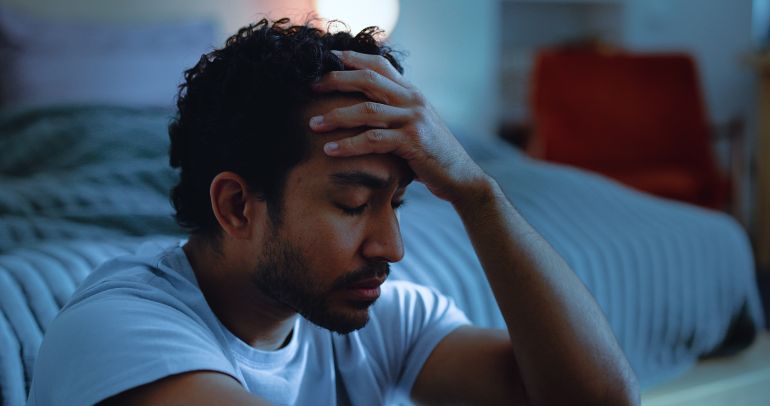Night, upset and man thinking with depression, mental health or insomnia from sad memories in bedroom. Late, contemplation and anxious person with grief, worry and sleepless from stress in apartment.