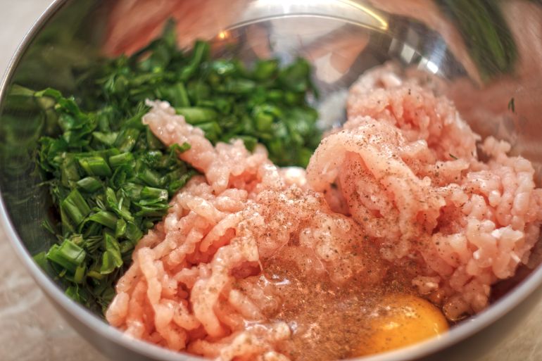 shutterstock_2727383351-1779265558 Metal bowl with raw minced meat, raw egg and chopped green onions. Process of making cutlets or meatballs.
