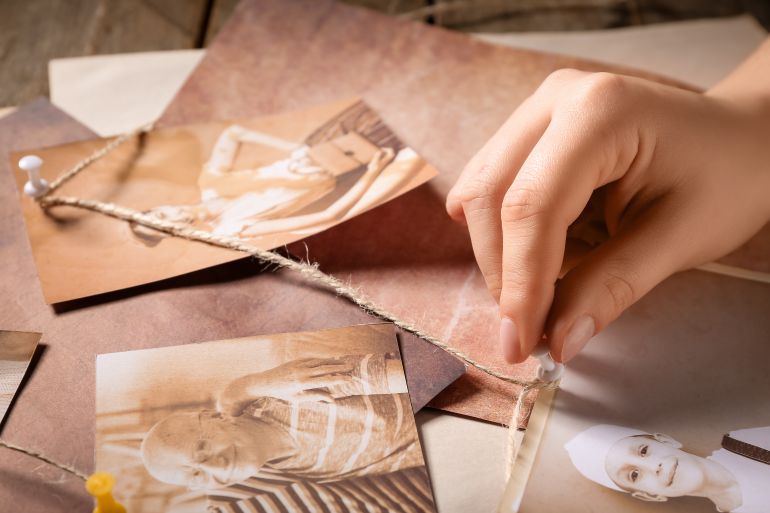 shutterstock_2757543159-1779709268 Hand of woman creating family tree with old photos of relatives