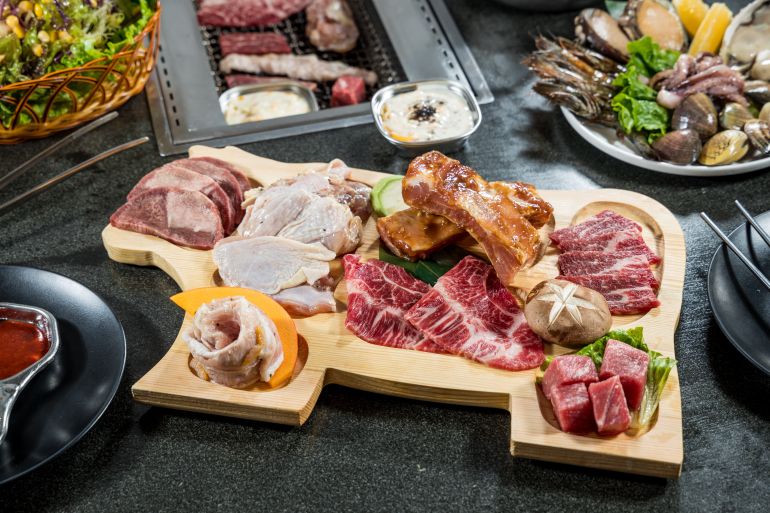 An overhead view of assorted raw meats arranged on a wooden board ready for grilling. The variety showcases premium cuts suitable for barbecue restaurants and grill menu promotion.