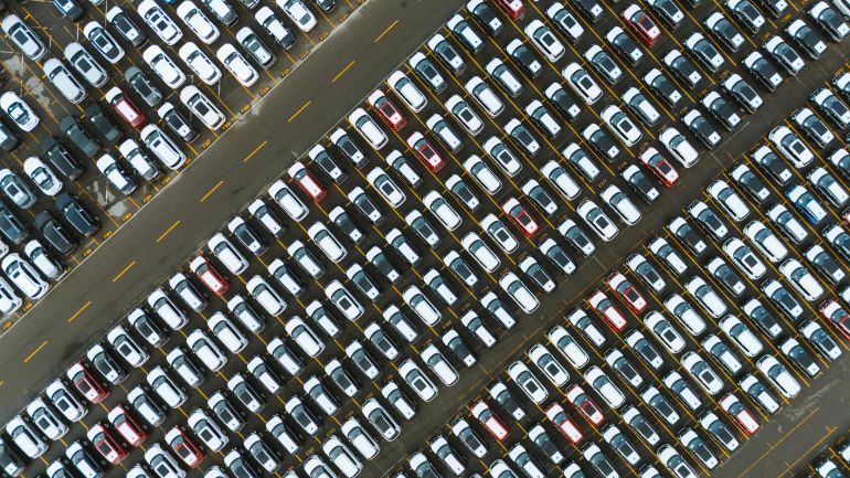 swq-alsyarat-1778940075 Aerial perspective of neatly parked cars in a large parking lot.