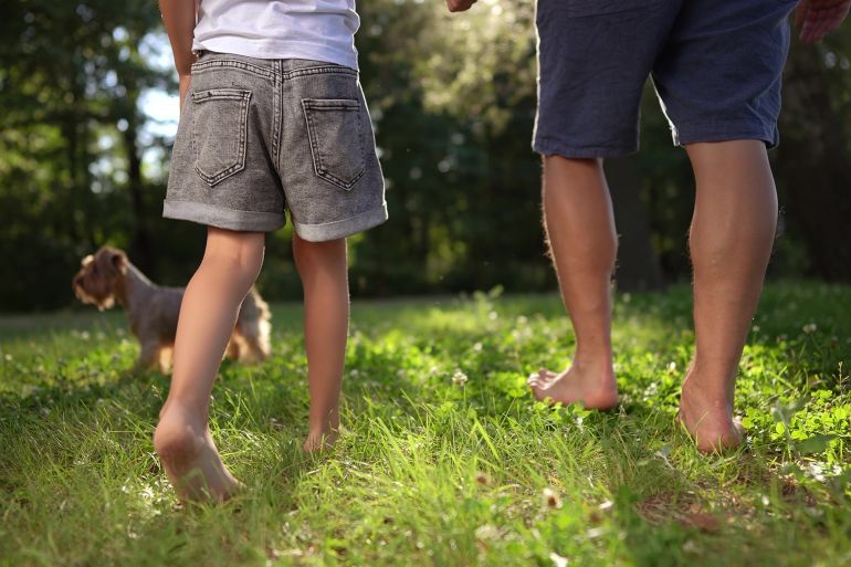 father and daughter walking in the park. happy family childhood dream concept. dad and daughter holding hands and walk barefoot on the grass. lifestyle dog running around. bare feet close up