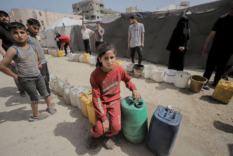 Palestinian children wait beside water containers at a displacement camp in the Rimal neighborhood of Gaza City on May 19, 2026. Palestinians in Gaza continue to face severe shortages of clean drinking water amid widespread damage to infrastructure and ongoing humanitarian challenges. (Photo by Ahmed Al Arini / Middle East Images / AFP via Getty Images)