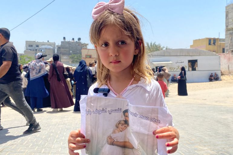 طفلة ترفع لافتة تطالب بحقها في رؤية والدها الذي يقيم خارج غزة منذ ما قبل اندلاع حرب الإبادة