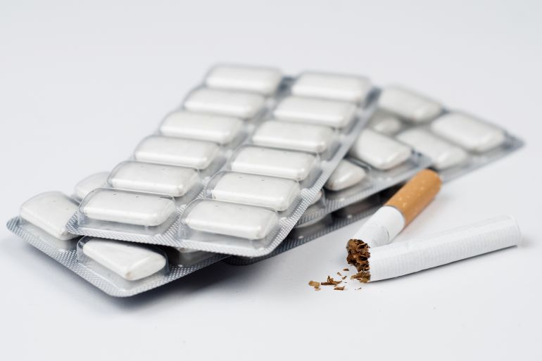 Broken cigarette in front of nicotine chewing gum disks.