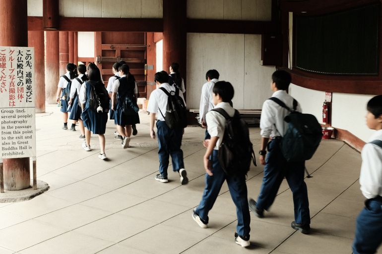 1schools-in-japan-1781604166 Students in uniform walking through a traditional building interior, Japan.