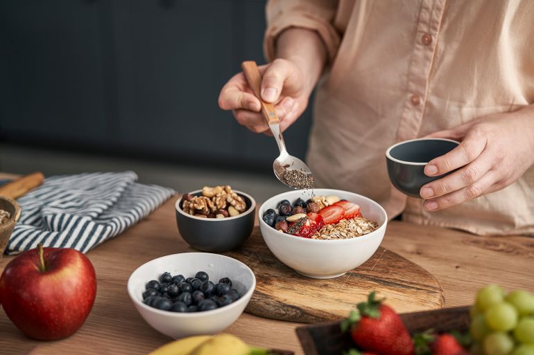 4-1780471998 Woman adding seeds to bowl of muesli