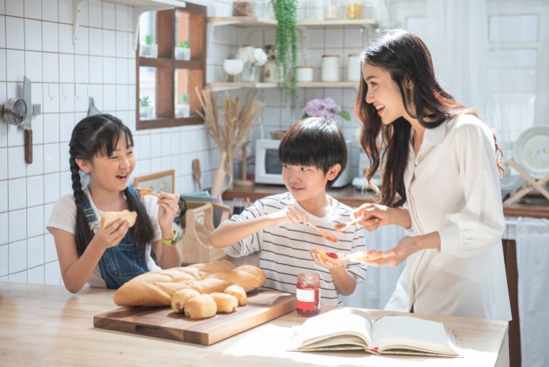 555-1689094411 Happy asian family in the kitchen. mother and son and daughter spread strawberry yam on bread, leisure activities at home.