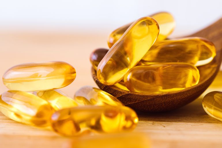 Close up the vitamin D and Omega 3 fish oil capsules supplement on wooden plate for good brain , heart and health eating benefit by Cozine @ادوبي ستوك