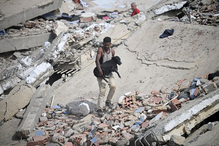 A volunteer carries a rescued dog across the rubble of a collapsed building following twin earthquakes in Caraballeda, La Guaira state, some 40 km northeast of Caracas, on June 25, 2026. The death toll from twin quakes, measured at magnitudes 7.2 and 7.5, has risen to at least 188, with more than 1,520 others injured, top lawmaker Jorge Rodriguez reported, while residents continue searching for missing relatives. (Photo by Federico PARRA / AFP)