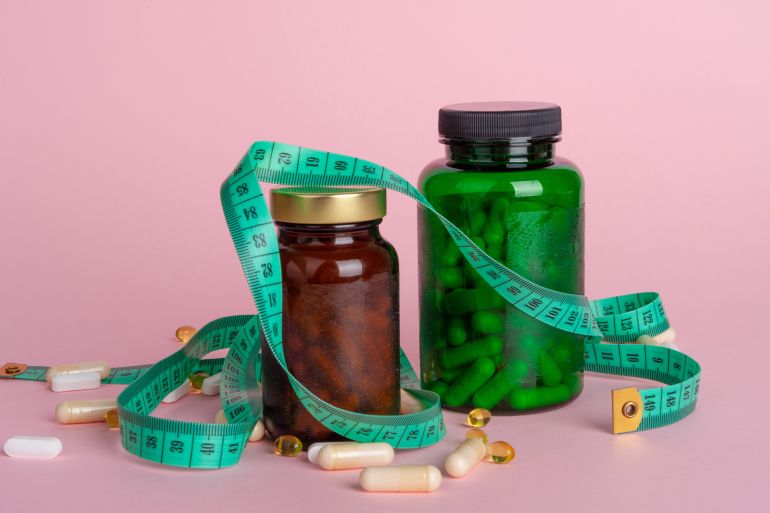 651-1771073477 Weight Loss Pill in Bottles, Measuring Tape, Diet Supplements Capsules, Obesity Lose Tablets, Color Drugs Pile, Weight Loss Pills on Pink Background with Copy Space for Text