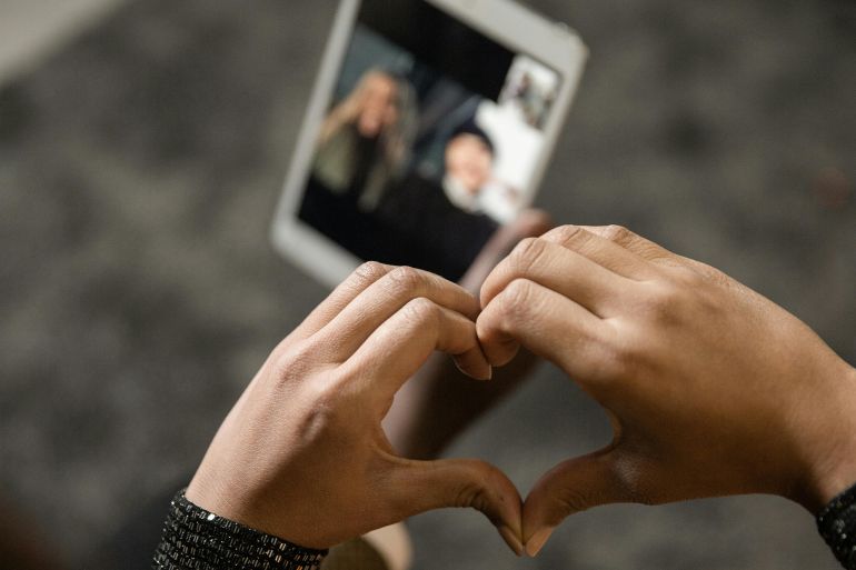 Close-up of hands forming a heart shape during a video call on a tablet.