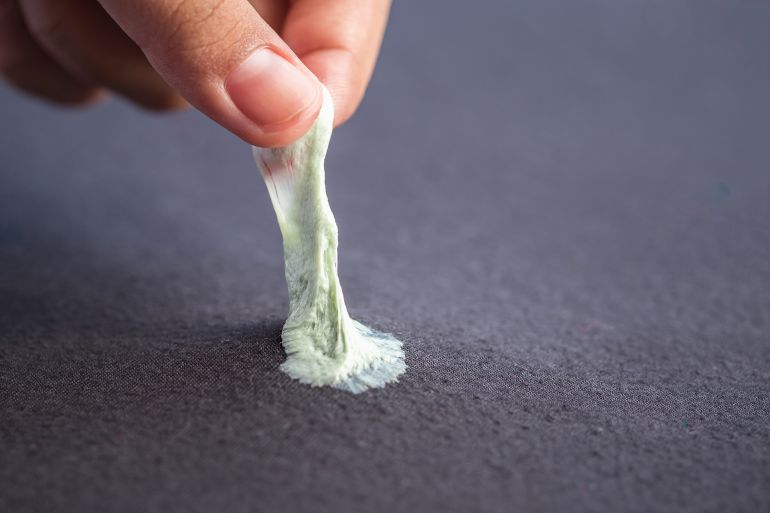 Hand removing sticky chewing gum from black textile or clothes by SKT Studio @ادوبي ستوك