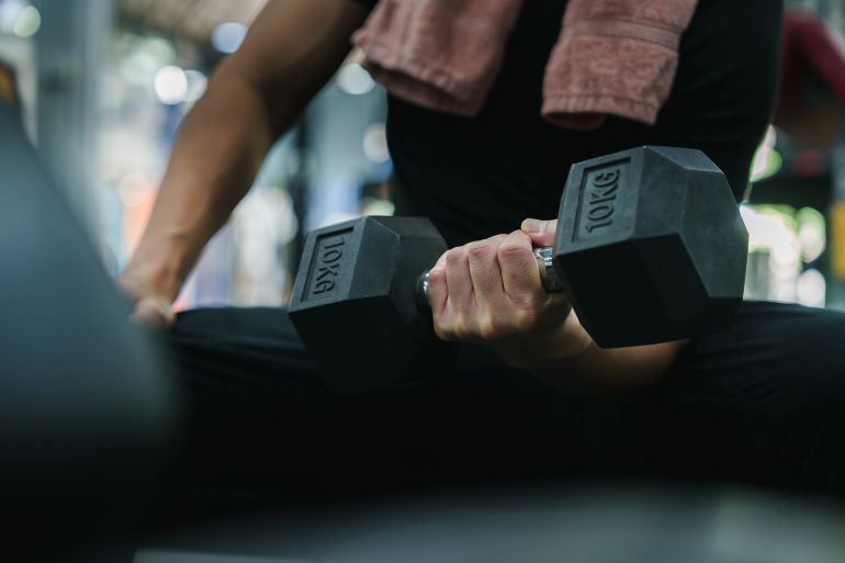 79-1782112303 A close-up shot of a man's hand firmly holding a 10kg dumbbell during a focused weightlifting session in a modern gym. The image highlights dedication to building strength and an active lifestyle.