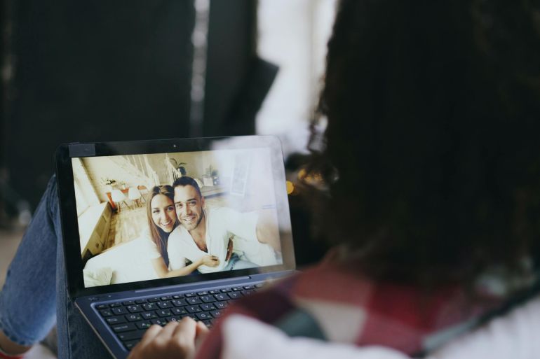 Woman viewing a happy couple's photo on a laptop at home, suggesting connection through technology.