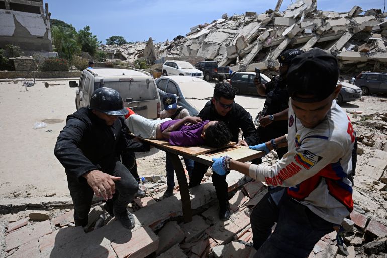 Rescuers carry an injured person on a makeshift stretcher past a large pile of rubble from a collapsed building following an earthquake in Los Corales, La Guaira state, about 38 km northwest of Caracas, on June 25, 2026. A twin earthquake that was Venezuela's largest in over a century has killed at least 188 people and destroyed multiple buildings near the capital, where residents searched on June 25 for missing relatives. (Photo by Federico PARRA / AFP)