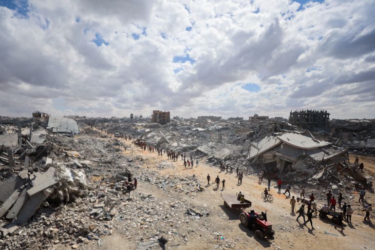 فلسطينيون يبحثون بين أنقاض المباني وسط دمار واسع جراء القصف الإسرائيلي في خان يونس جنوبي قطاع غزة في 12 أكتوبر/تشرين الأول 2025.