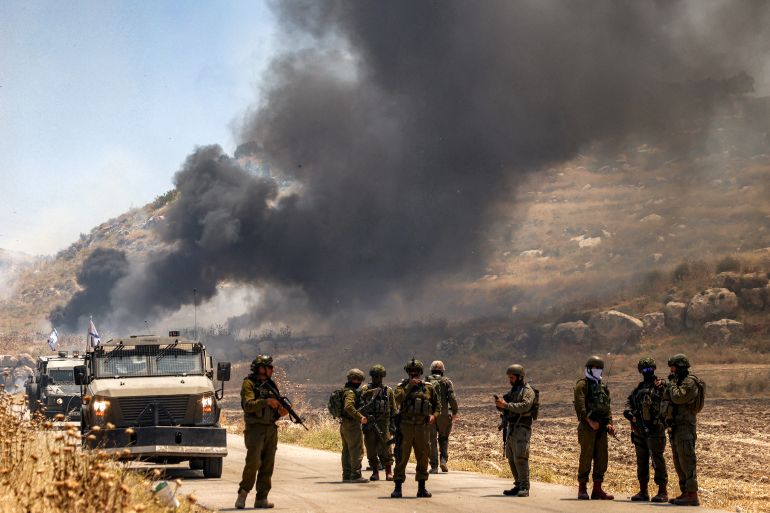 afp_6a2376f7b872-1780709111-1 TOPSHOT - Israeli security forces stand guard along a road while behind smoke billows from an area reportedly set ablaze by Israeli settlers in the Palestinian village of Idna, west of Hebron in the occupied West Bank, on June 5, 2026.