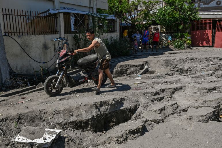 afp_6a280680c171-1781008000 A man pushes a motorcycle along a damaged road after a 7.8 magnitude earthquake in General Santos City on June 9, 2026.