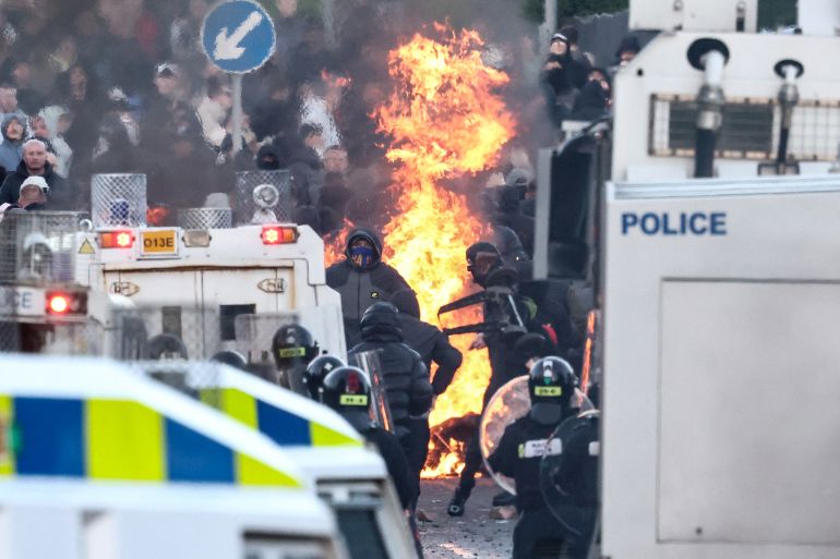 afp_6a2a39a6a2fe-1781152166 Protesters (behind) stand off with police as the former block a road leading to a hotel previously believed to house migrants, in Glengormley, north of Belfast, Northern Ireland, on June 10, 2026.