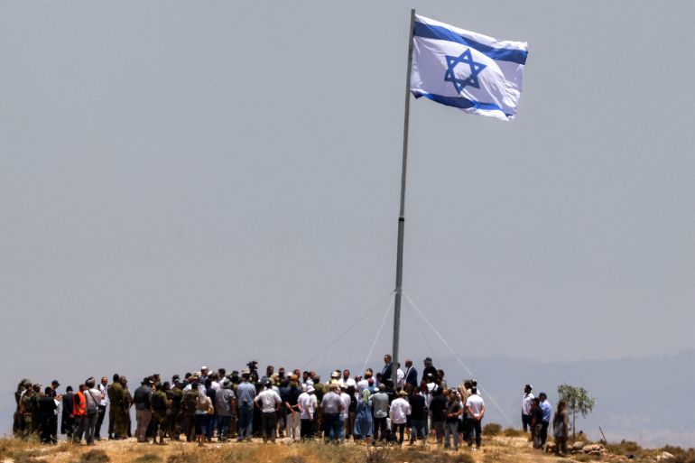 afp_6a323039b233-1781674041 Israeli settlers, accompanied by Israel's far-right finance minister Bezalel Smotrich, raise a large Israeli flag during a cornerstone laying ceremony for a new settlement on Mount Tarousa, near the town of Dura west of Hebron in the occupied West Bank, on June 16, 2026.