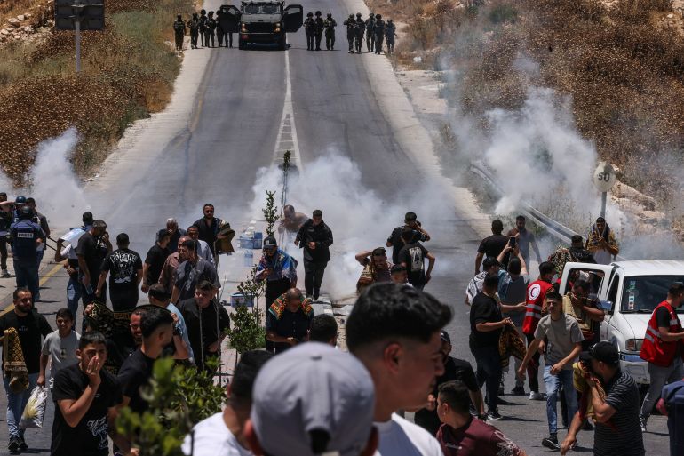 afp_6a35404af28e-1781874763 Protesters and local Palestinian landowners, who say some of their land was taken for the newly built Mount Tarousa settlement (background), run from tear gas fired by Israeli security forces blocking a road leading to the hilltop during a rally against the settlement near Dura in the Israeli-occupied West Bank on June 19, 2026.