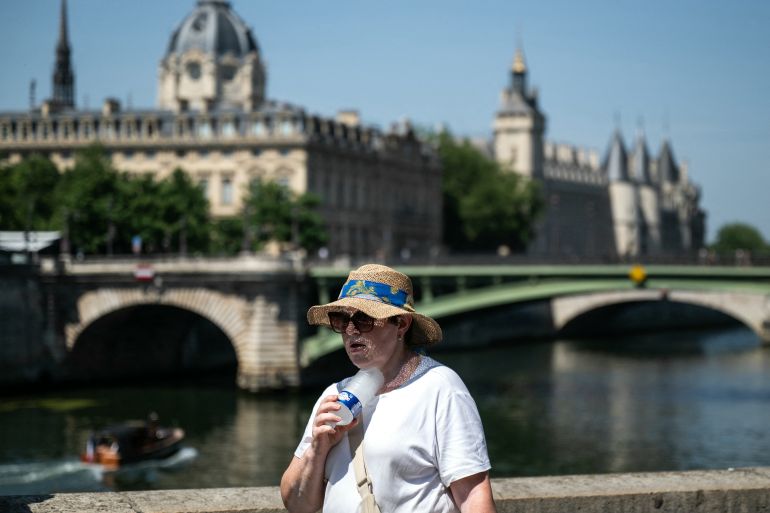 afp_6a3904af5b25-1782121647 TOPSHOT - A woman with a hat cools off with a cold bottle of water on the Seine riverside with the Paris commercial court (L) and the Conciergerie buildings and the Pont Notre Dame in the background as France experiences a heat wave in Paris, France, on June 21, 2026.