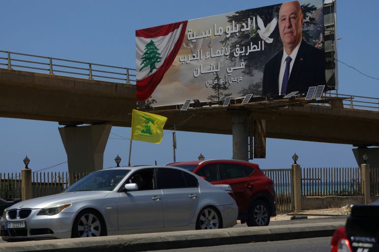 A yellow Hezbollah flag flutters from the rooftop of a car as it drives towards southern Lebanon, past a billboard on which hangs a portrait of Lebanese President Joseph Aoun and reads, 'Diplomacy is the way to end wat in Lebanon' in the coastal city of Sidon, south of the Lebanese capital Beirut on June 15, 2026.