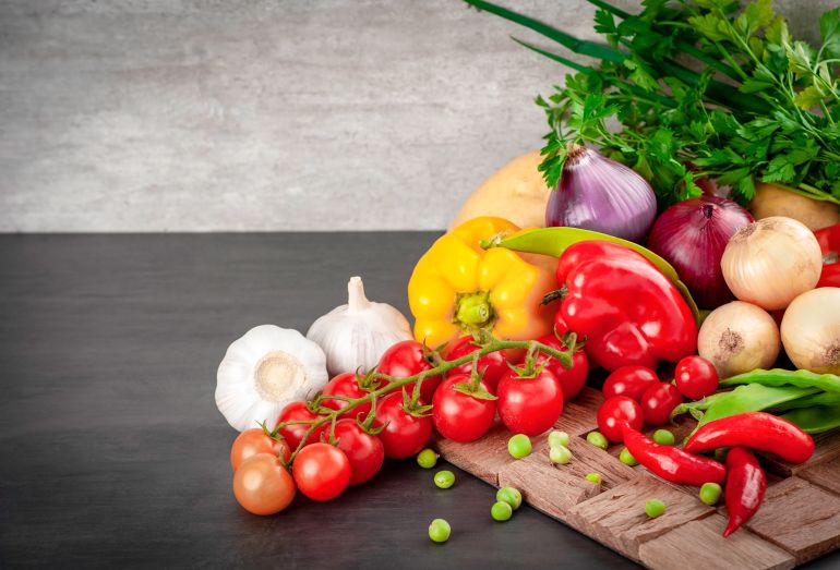 alakl-1779694589 A vibrant selection of fresh vegetables including bell peppers and tomatoes on a wooden board.