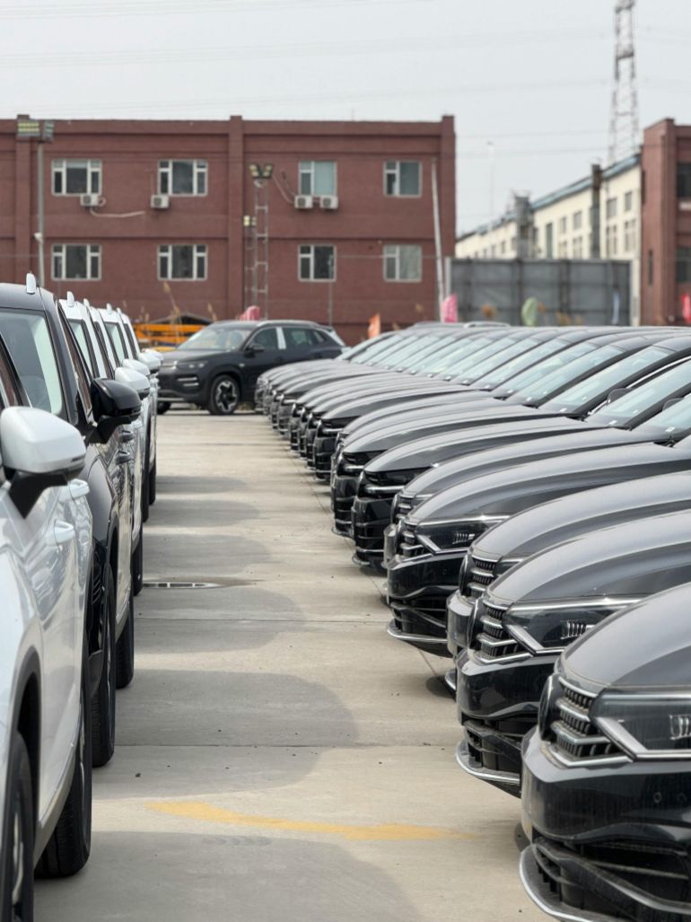 alsyny-1779705871-2 A view of modern cars neatly parked in an industrial lot on a cloudy day.