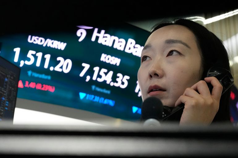A currency trader talks on the phone near a screen showing the Korea Composite Stock Price Index (KOSPI) and the foreign exchange rate between U.S. dollar and South Korean won, left, at the foreign exchange dealing room of the Hana Bank headquarters in Seoul, South Korea, Wednesday, May 20, 2026. (AP Photo/Ahn Young-joon)