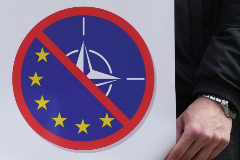 A man holds a banner against EU and NATO during a protest against NATO in front of the former Serbian army headquarters, destroyed during NATO's bombing campaign 26 years ago (March 24. to June 10. 1999) in Belgrade, Serbia, Sunday, March 23, 2025. (AP Photo/Darko Vojinovic)