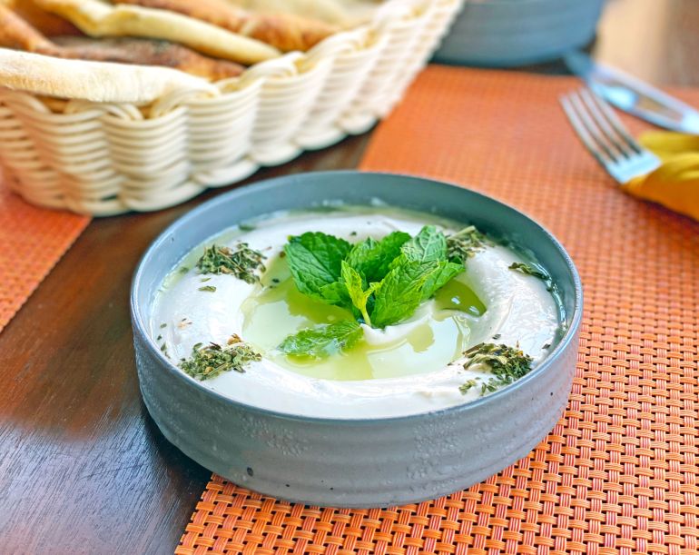 Delicious tzatziki dip garnished with mint leaves served in a bowl, perfect for a refreshing snack.