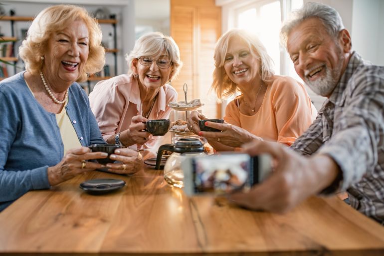 d8b4d98ad8aed988d8aed8a9-d8b3d8b9d98ad8afd8a9-1776182125 Group of happy mature friends having fun while gathering at home and taking selfie with smart phone.
