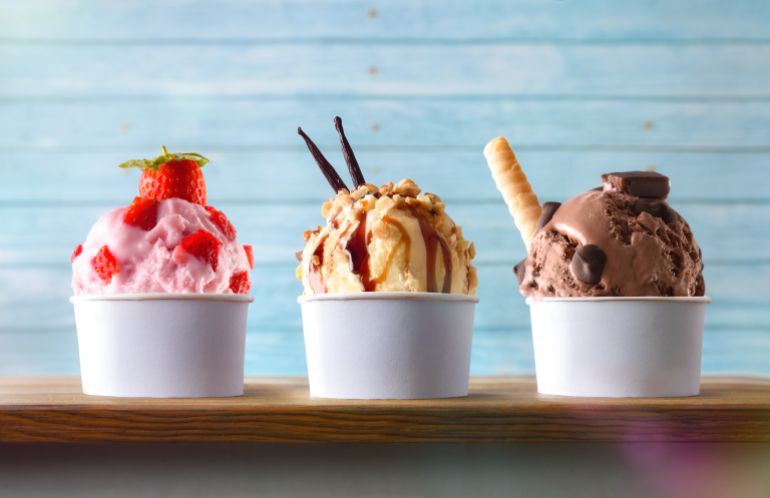 Three glasses of ice cream with strawberry, vanilla and chocolate balls decorated on a wooden table and blue slatted background. Front view.
