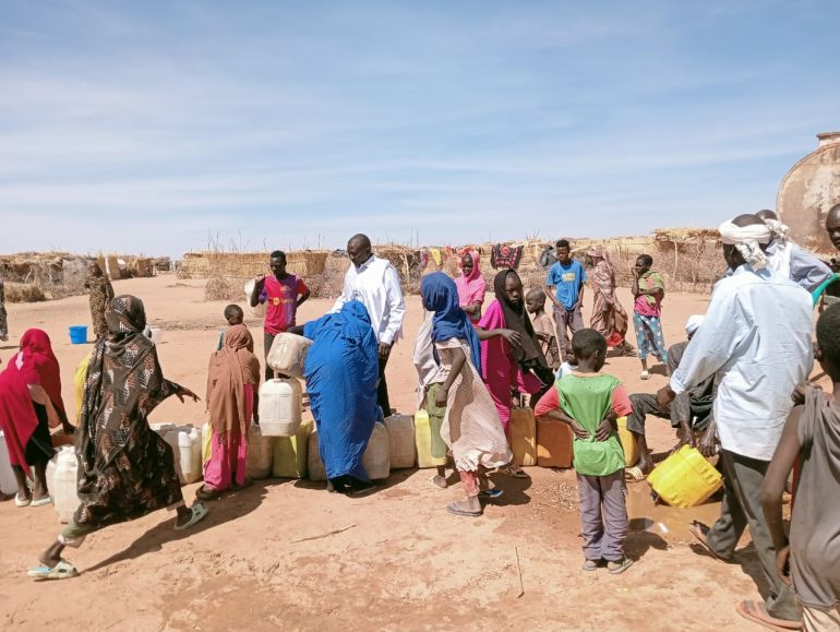 طابور طويل من النازحين يمتد تحت الشمس، ينتظرون دورهم للحصول على جراكنهم ـ الجزيرة نت_