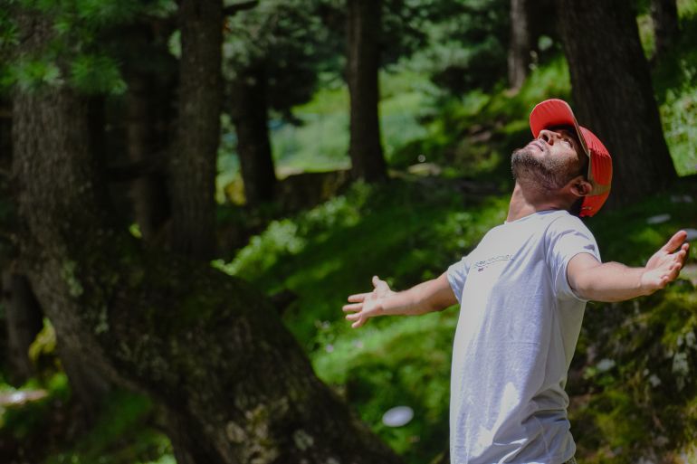 dhsht-tbycabft-1781713891 Man with open arms enjoying the serene beauty of a lush green forest.