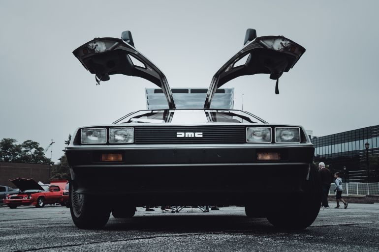 dyy-1780730580 Front view of a vintage DeLorean car with its distinctive gullwing doors open, displayed outdoors.