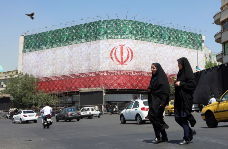 epa_6a2f318e9961-1781477774 epa13035937 Veiled Iranian women walk past a billboard featuring Iran's national flag at Enqelab Square in Tehran, Iran, 14 June 2026. US President Donald Trump saying on a social media platform that a deal could be signed soon. EPA/ABEDIN TAHERKENAREH RESTRICTIONS: NO Access Israel Media/Persian Language TV Stations Outside Iran/Strictly No Access BBC Persian/VOA Persian/Manoto TV/Iran International TV. (As mandated by Iran's Directorate General for Foreign Media) --