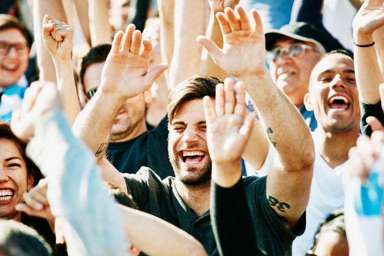 fscda12-1781278544 Laughing man cheering with crowd in stadium - stock photo Laughing man with arms raised overhead cheering with crowd in stadium at sporting event