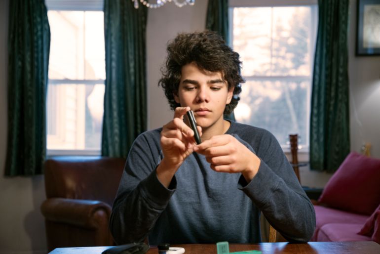 gettyimages-1359347886 A teenaged diabetes patient checking his blood sugar at home. Juvenile diabetes concept.
