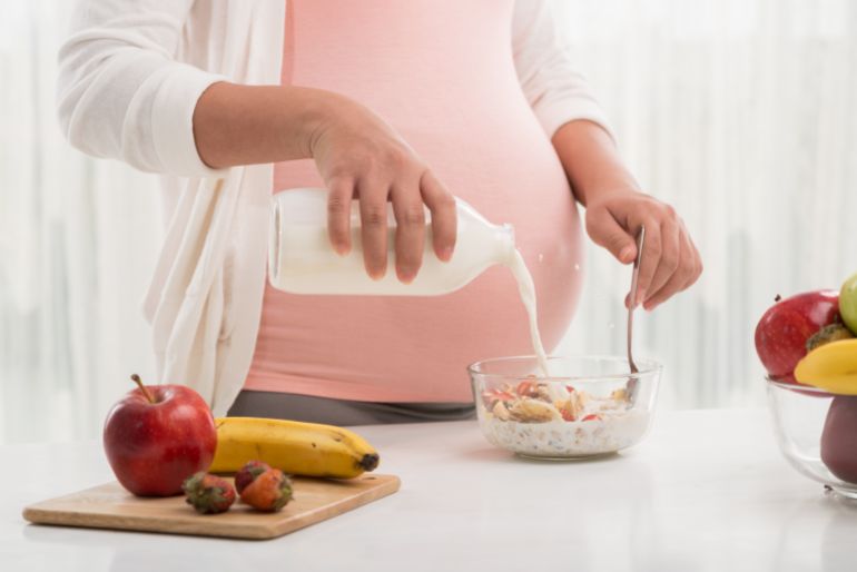 gettyimages-490262643-1728748509 Pregnant woman pouring milk into her bowl with fruit fresh