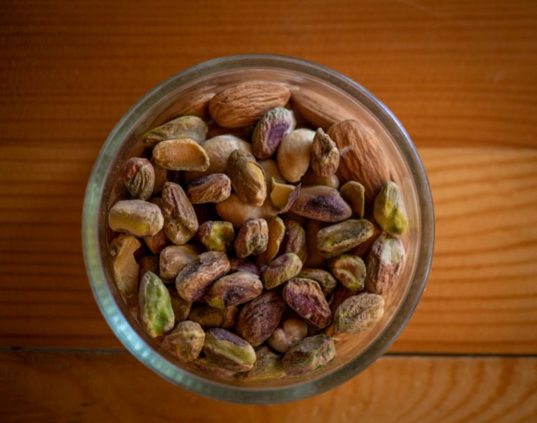 mksrat-1779695005 A close-up top view of assorted nuts in a glass bowl on a wooden table, highlighting natural textures.