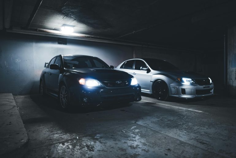 Subaru WRX and Impreza parked in a dimly lit underground garage.