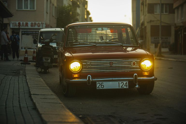 A retro VAZ-2101 with headlights on parked on a moody city street, capturing an urban vintage vibe.